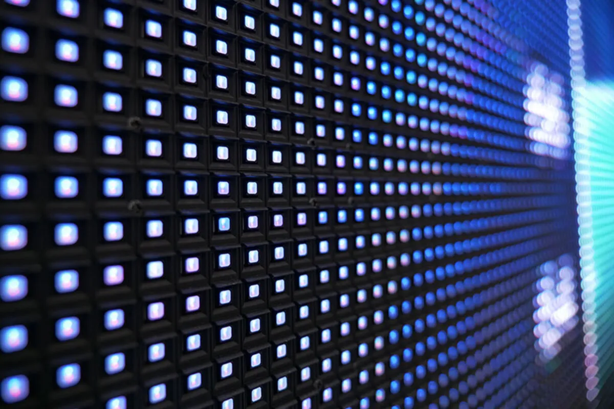 Close-up de um painel de LED com pixels quadrados acendendo em cores azuis e roxas, criando uma grade de luzes e um efeito de profundidade, ideal para tecnologia de display e sinalização.