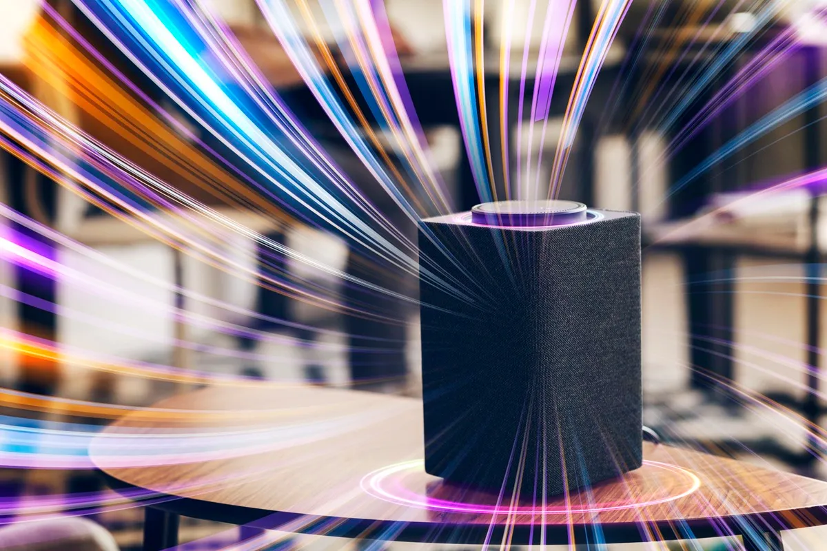 Caixa de som inteligente preta sobre mesa de madeira com efeitos de luz coloridos em movimento