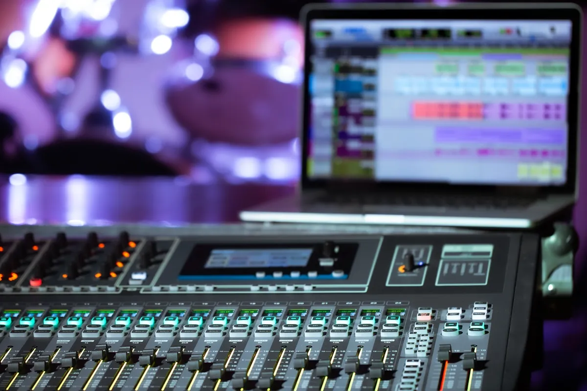 Mesa de som profissional com sliders e luzes coloridas em um ambiente iluminado, utilizada para controle de áudio em eventos ao vivo.