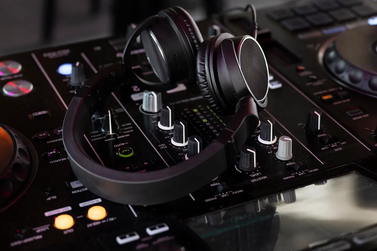 Fones de ouvido apoiados sobre uma mesa de som profissional com botões, luzes e controles de mixagem, utilizados em eventos e produções musicais.