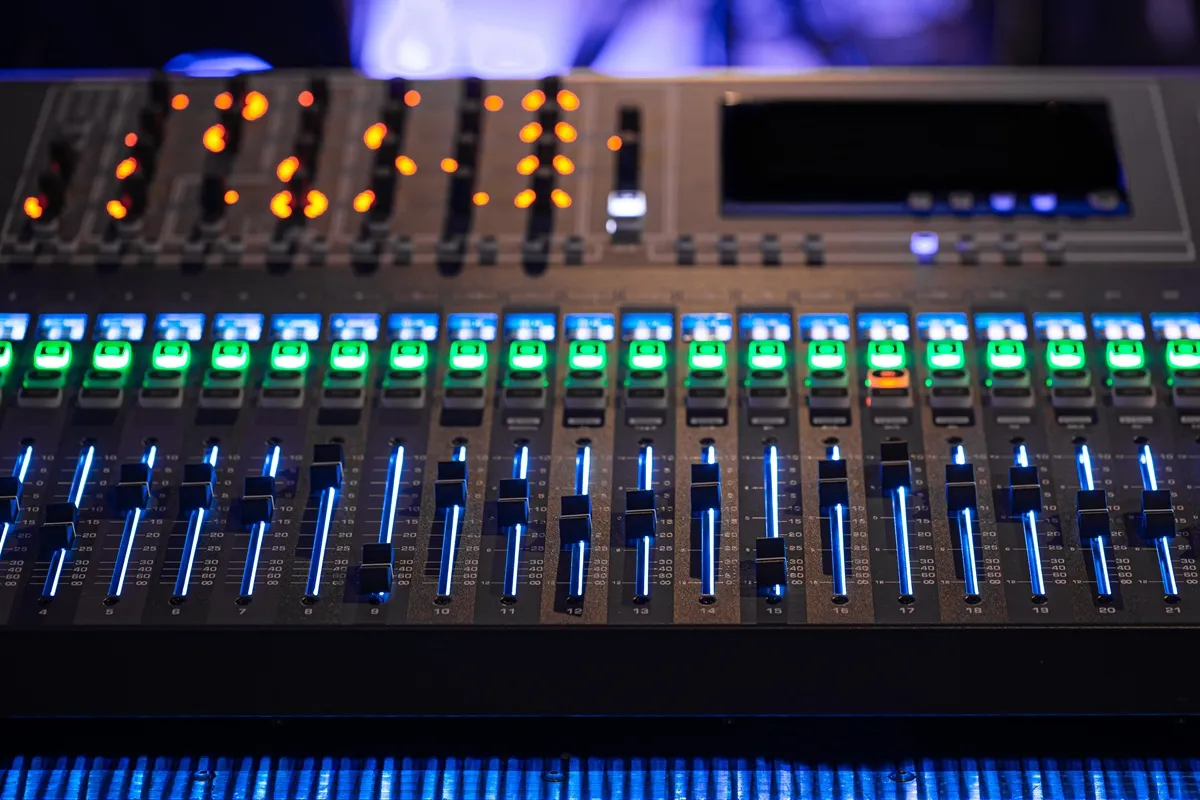 Mesa de som digital profissional com faders iluminados em azul e botões verdes, usada para mixagem de áudio ao vivo.