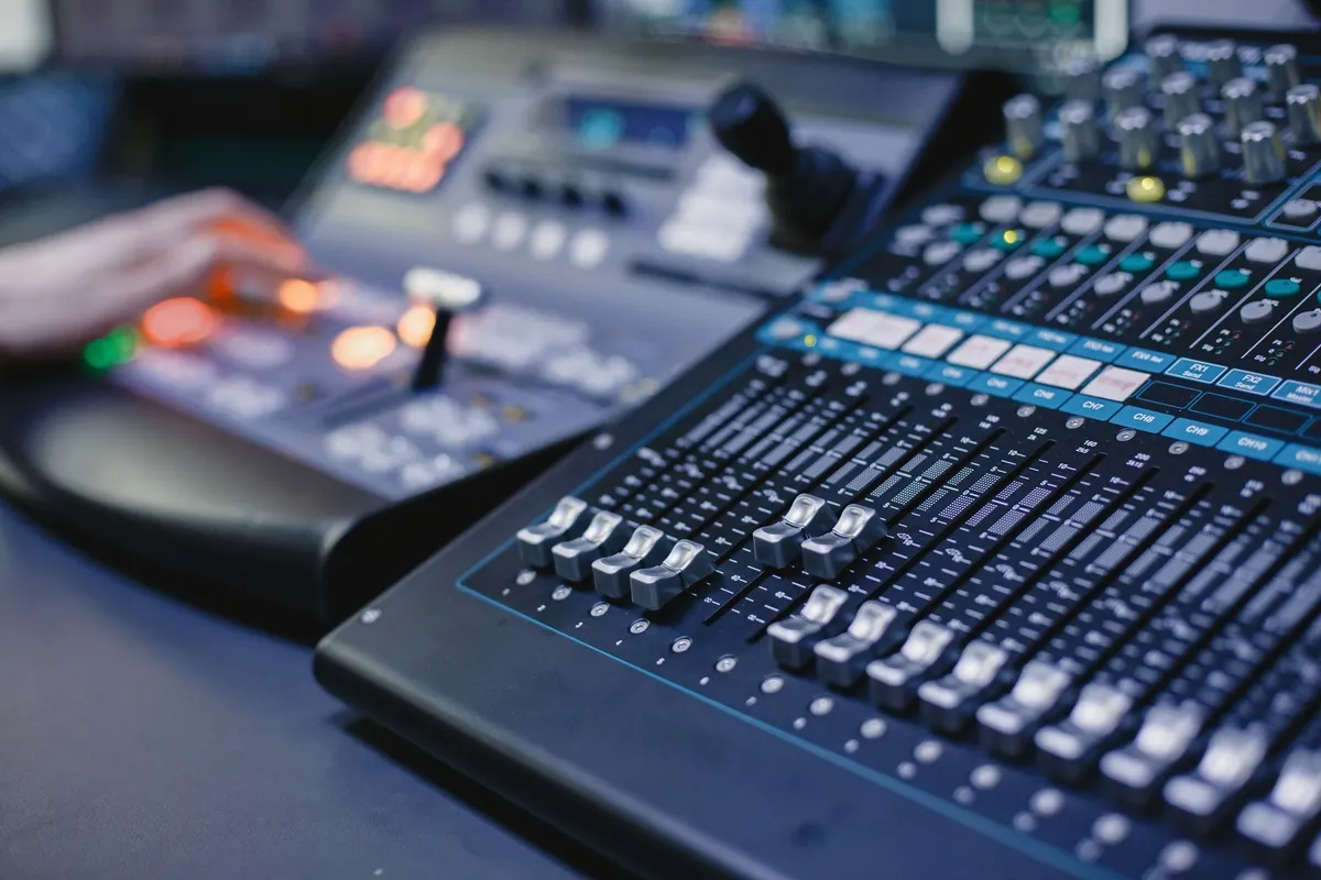 Mesa de som digital com faders metálicos, botões iluminados e painel de controle em funcionamento em estúdio de áudio.