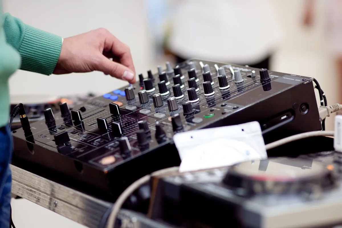 DJ ajustando controles de uma mesa de som profissional com diversos botões e potenciômetros.