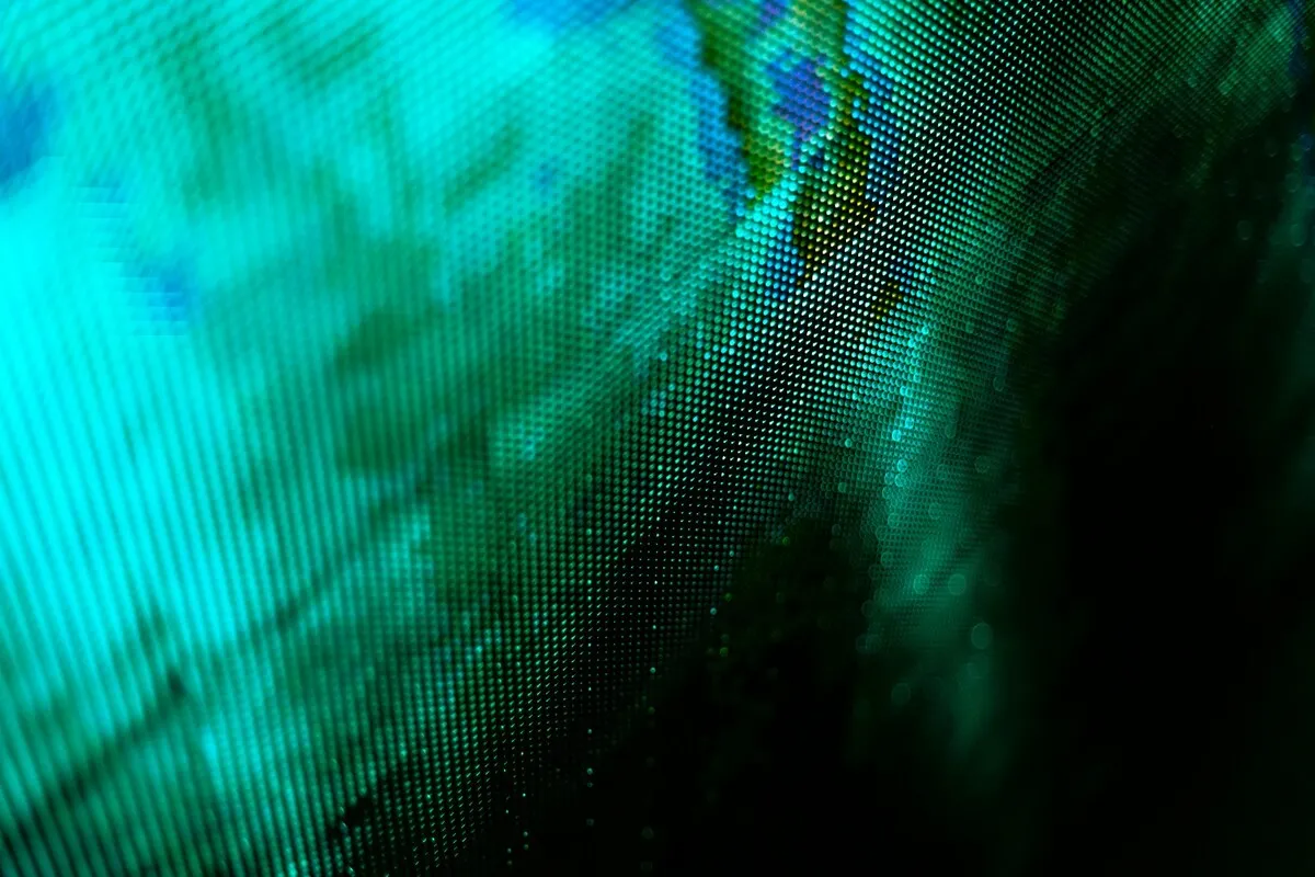 Close-up em ângulo diagonal de um telão de LED (pixel pitch) mostrando a grade de pixels em cores turquesa, verde e azul, com partes em contraste escuro.