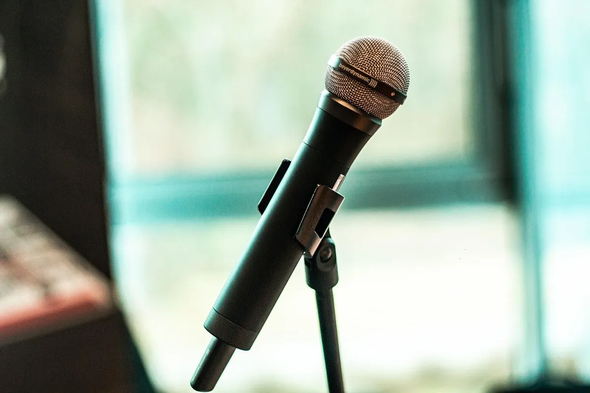 Close-up de um microfone sem fio de mão em um pedestal, com fundo desfocado e iluminação clara.