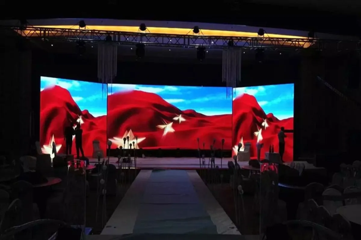 Palco com grande painel de LED indoor exibindo imagem colorida com montanhas vermelhas e céu azul em evento fechado.