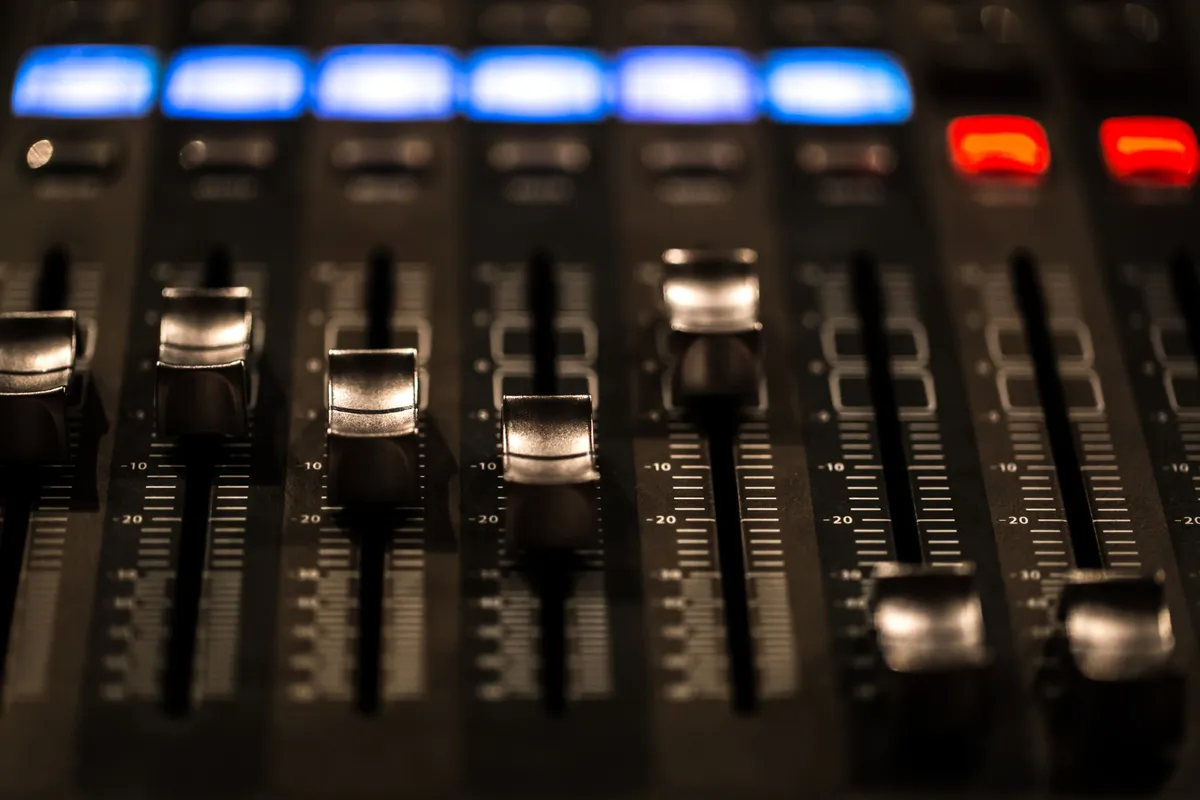 Close-up dos faders e botões iluminados de uma mesa de mixagem digital, parte essencial de um sistema de som de estúdio ou palco.