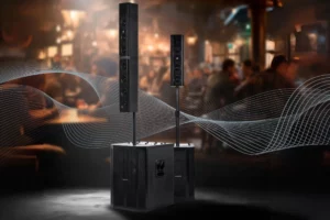 Sistema de som ambiente profissional modular (colunas line array e subwoofer) em um palco ou salão com iluminação dramática.