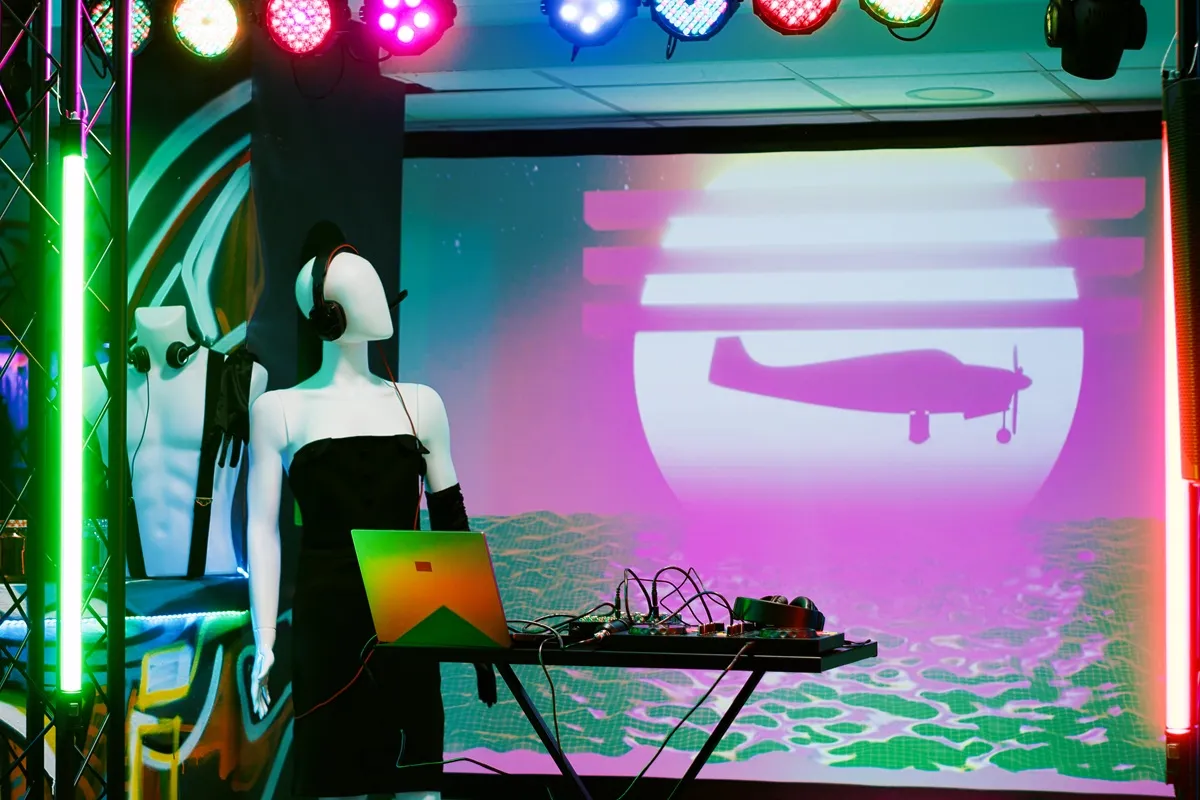 Cenrio iluminado com manequins usando fones de ouvido, mesa de DJ com laptop e telo de LED exibindo arte digital em tons neon.