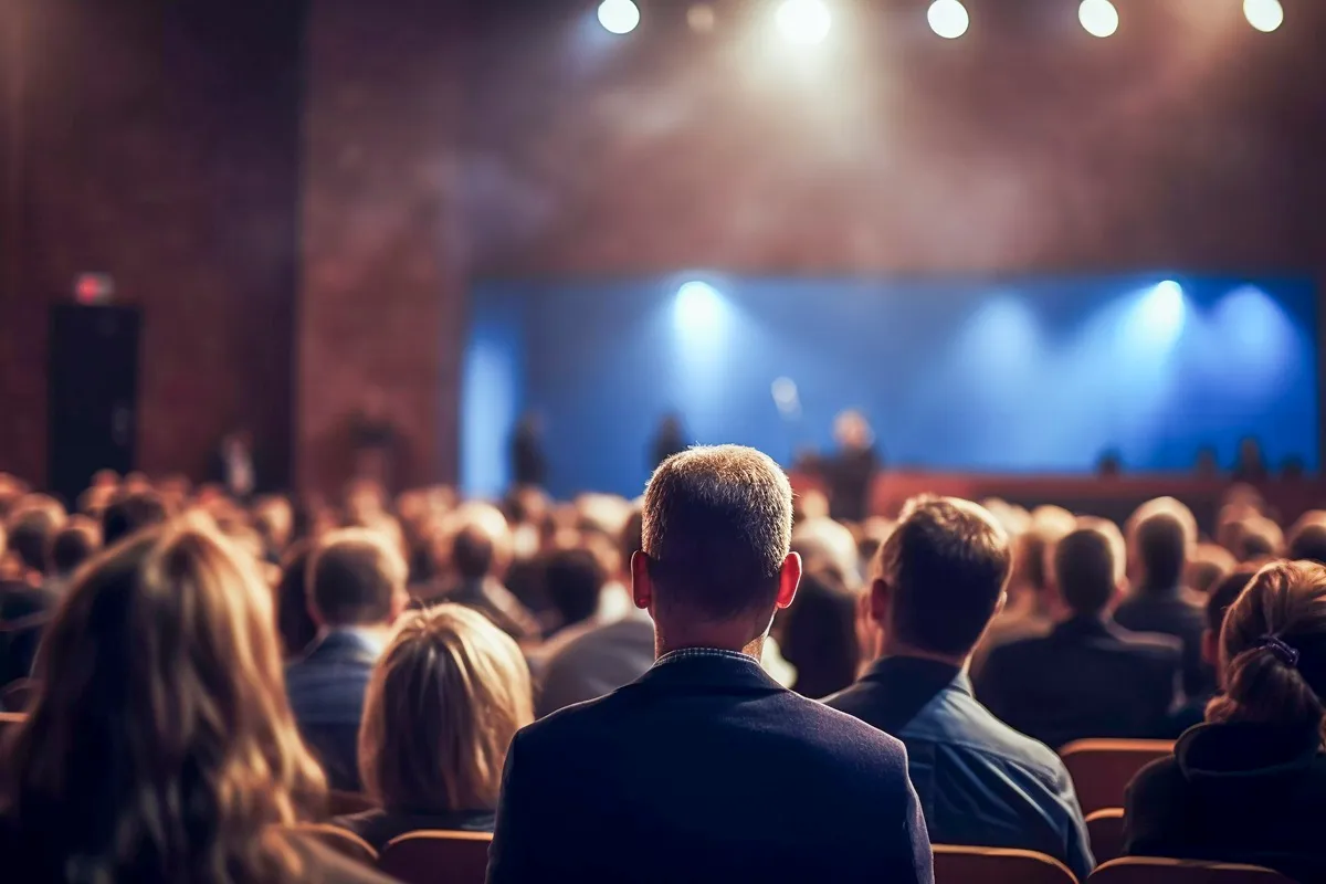 Plateia reunida em auditório assistindo a uma apresentação no palco iluminado.