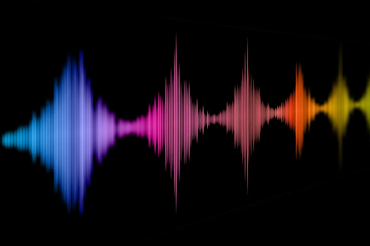 Ilustração de um equalizador de som exibindo ondas coloridas em azul, rosa, laranja e amarelo sobre fundo preto, formando um espectro de frequências.