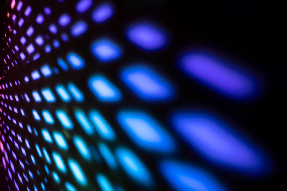 Luzes UV em tons de azul e roxo formando um padrão abstrato de pontos e traços luminosos sobre fundo escuro.