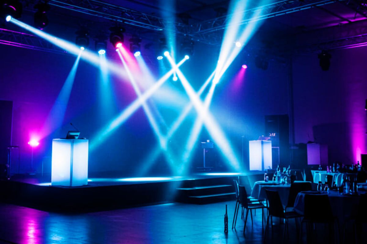 Palco vazio iluminado com luzes coloridas em azul, roxo e rosa durante a preparação de um evento