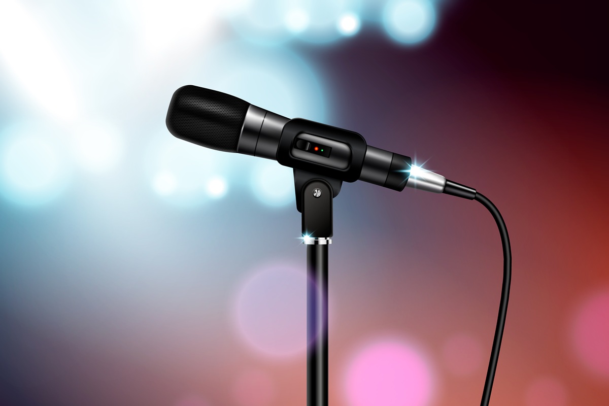 Microfone profissional preto em pedestal, com cabo conectado, iluminado por luzes coloridas de palco, ideal para podcasts, gravações de áudio e apresentações ao vivo