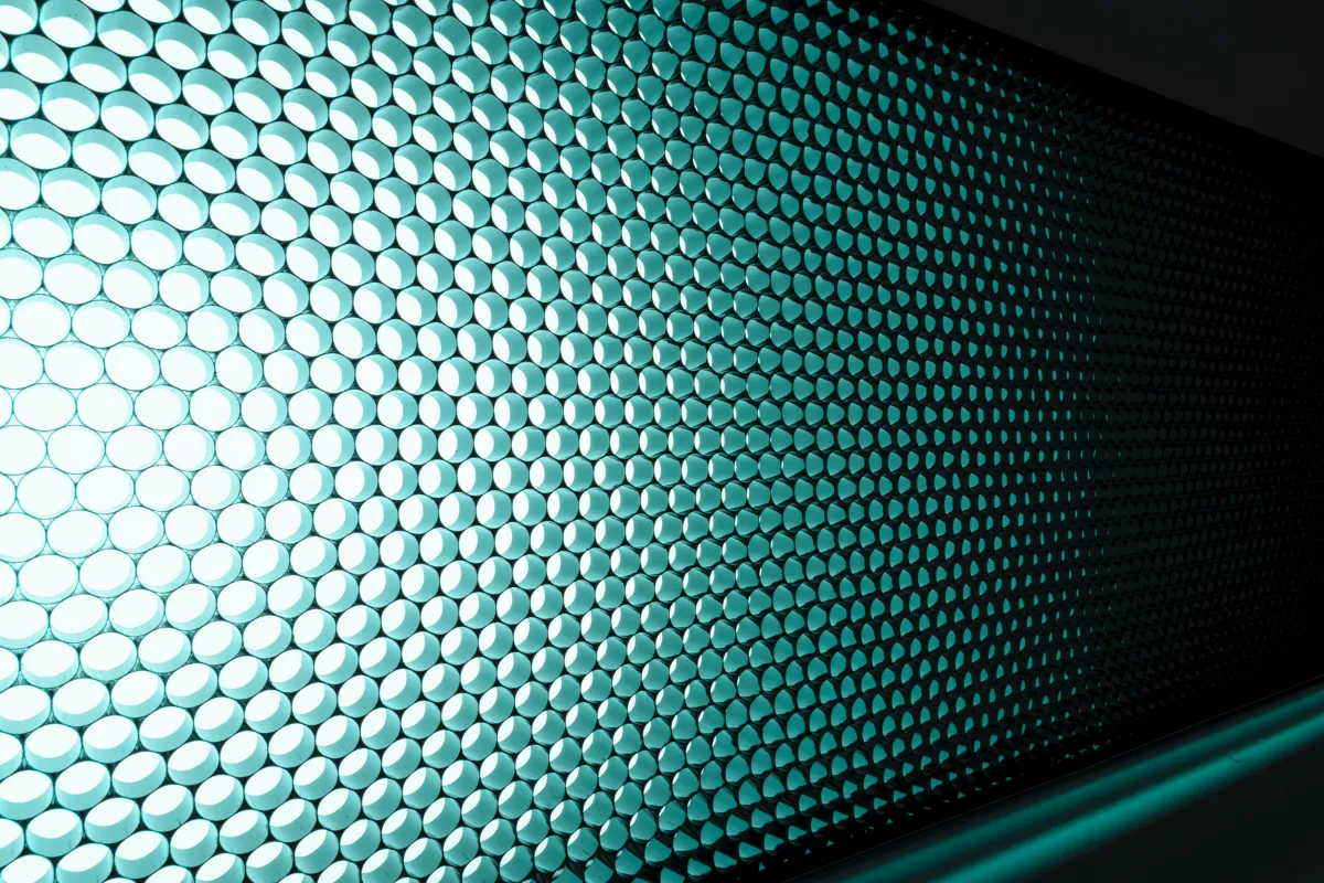 Parede com painel de iluminação formado por várias células circulares iluminadas em tom azul-esverdeado.
