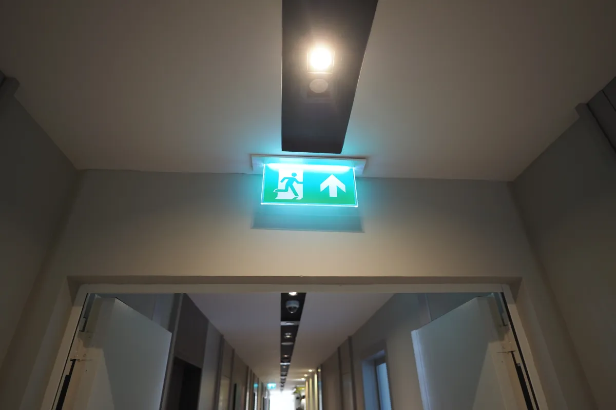 corredor com luz de emergência acesa e placa indicando saída acima da porta