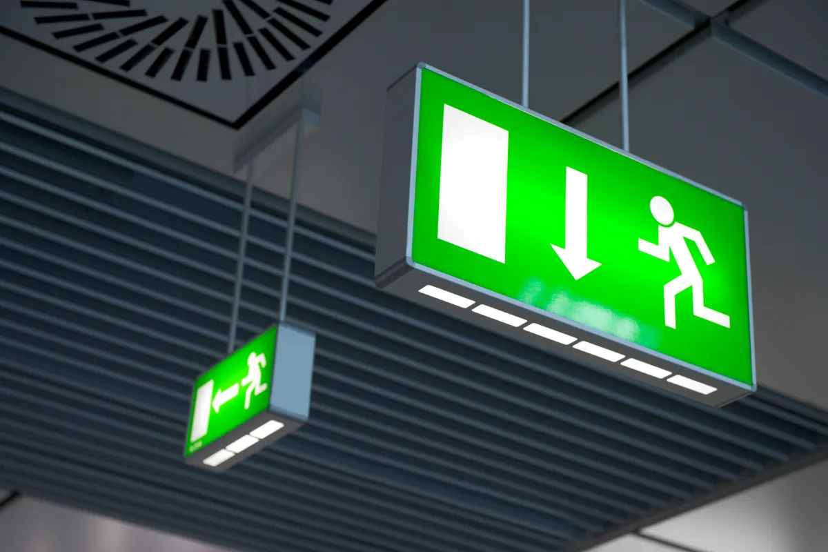placas verdes iluminadas de saída de emergência suspensas no teto com símbolo de evacuação