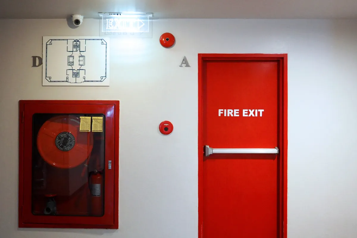 porta vermelha de saída de emergência com placa fire exit e equipamento de incêndio ao lado