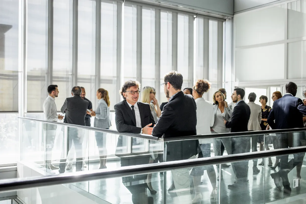 Grupo de profissionais conversando durante um evento corporativo em um espaço moderno com grandes janelas.