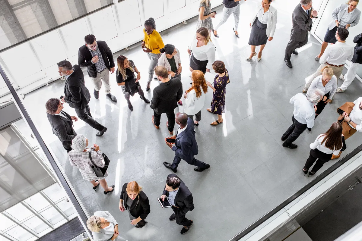 Vista de cima de pessoas conversando e circulando durante um evento corporativo em um espaço moderno.