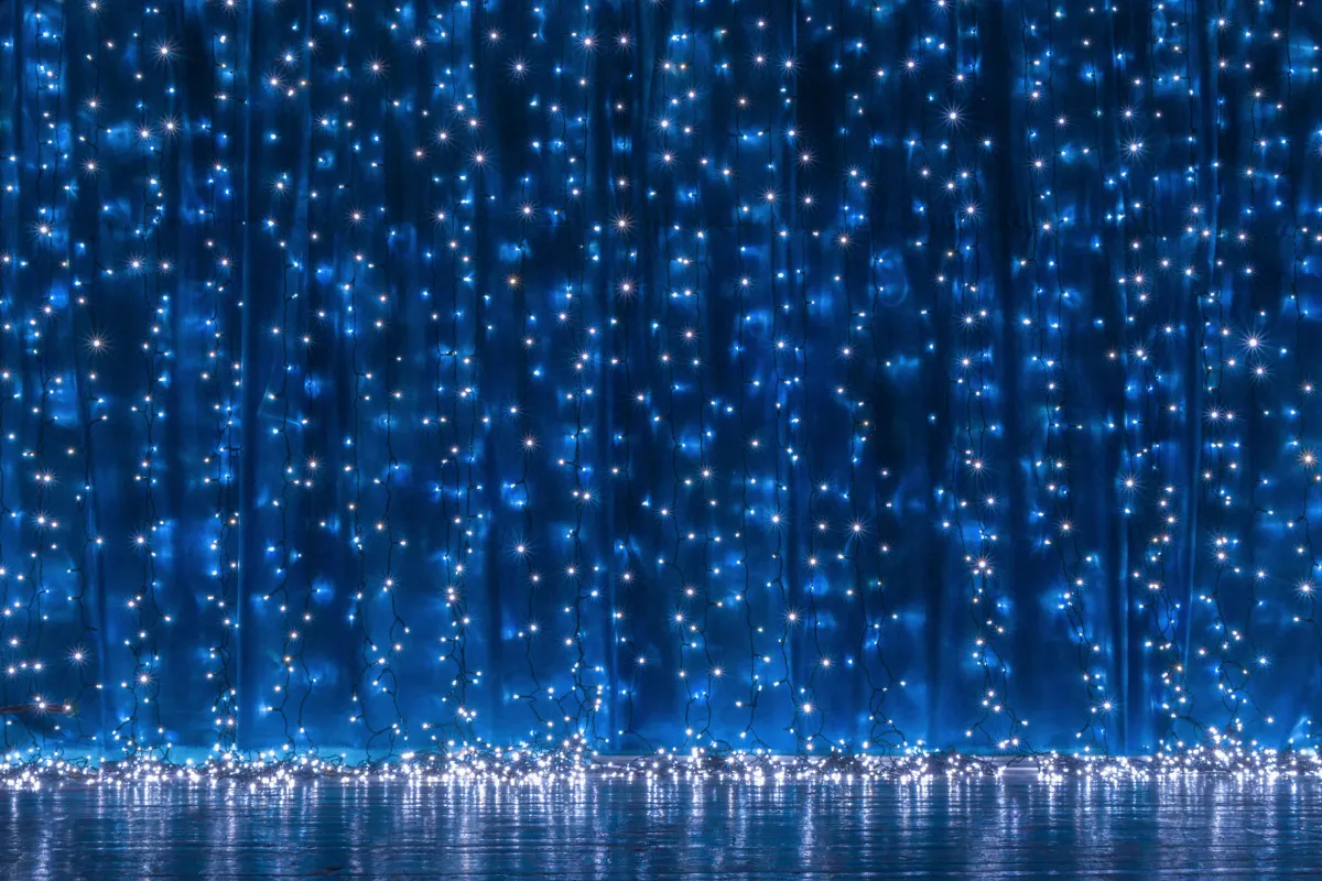 Cortina azul iluminada com fios de luzes brancas formando pequenos pontos brilhantes sobre fundo escuro.