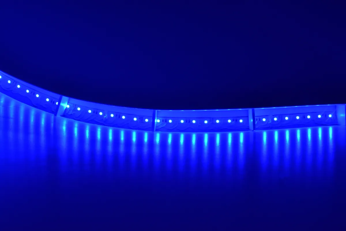 Fita de LED azul acesa formando uma curva sobre superfície refletiva com feixes de luz visíveis.
