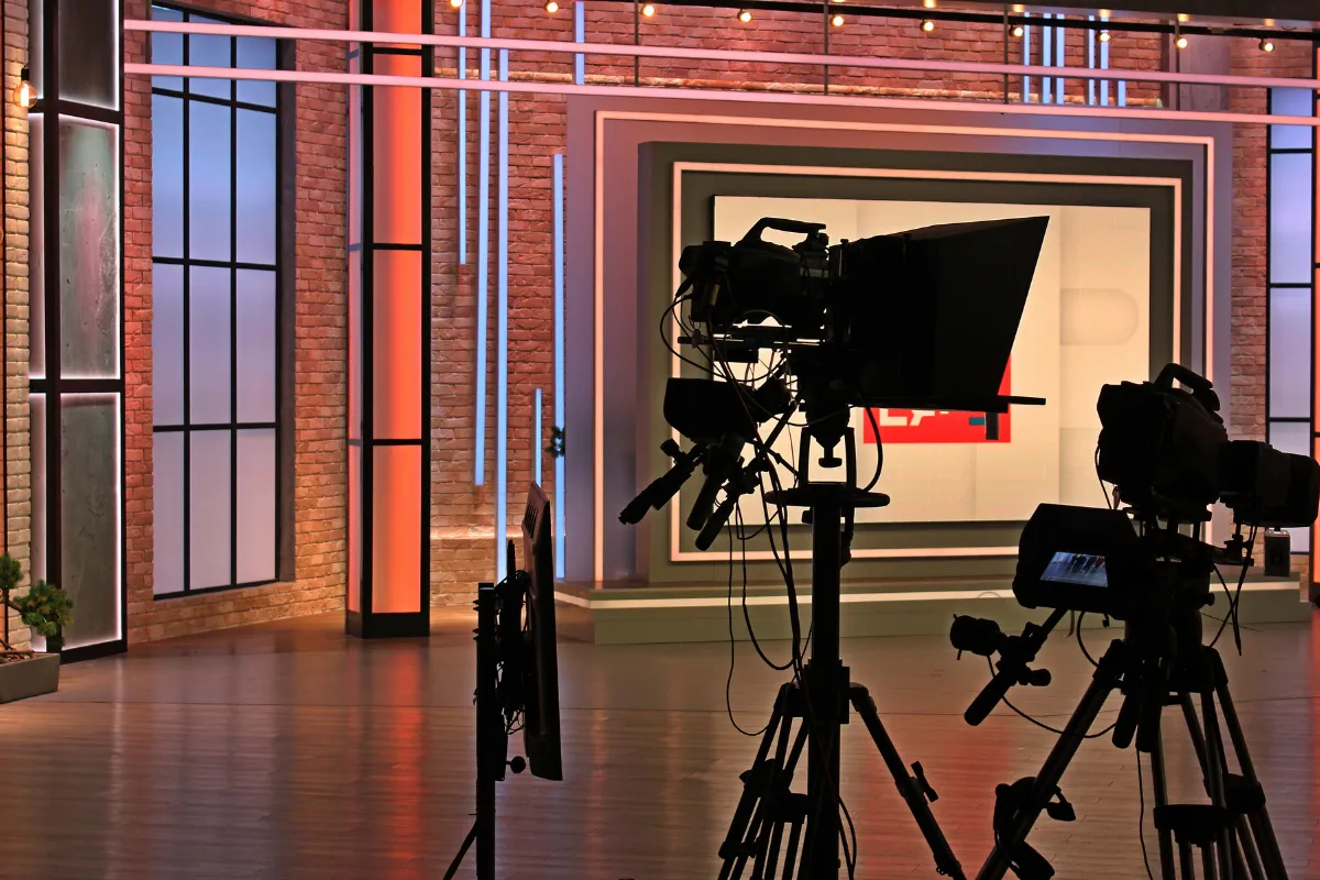 Câmeras profissionais posicionadas em um estúdio de televisão preparado para gravação de programa audiovisual.