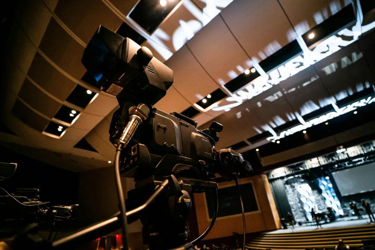 Câmera profissional montada em tripé dentro de um auditório preparada para gravação de um evento.