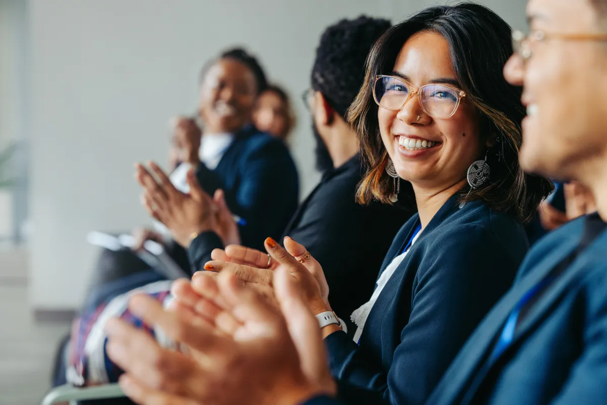 Participantes sentados aplaudindo durante uma apresentação em evento corporativo