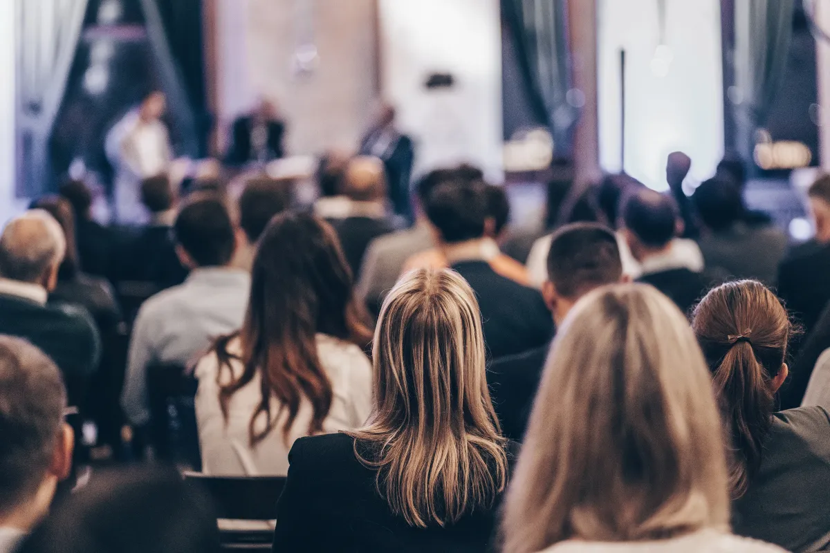 Público sentado em auditório assistindo a uma apresentação durante conferência corporativa.