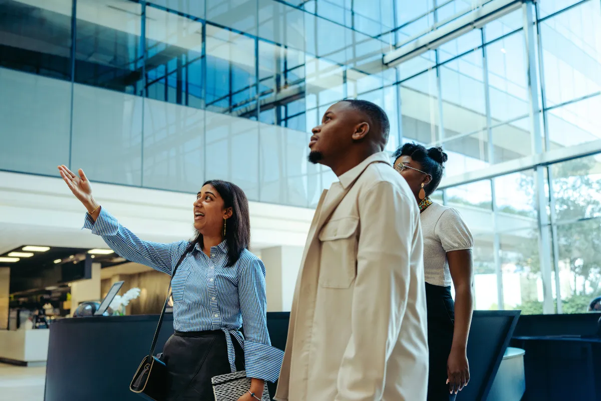 Grupo de pessoas em ambiente corporativo moderno enquanto uma mulher aponta e apresenta o local