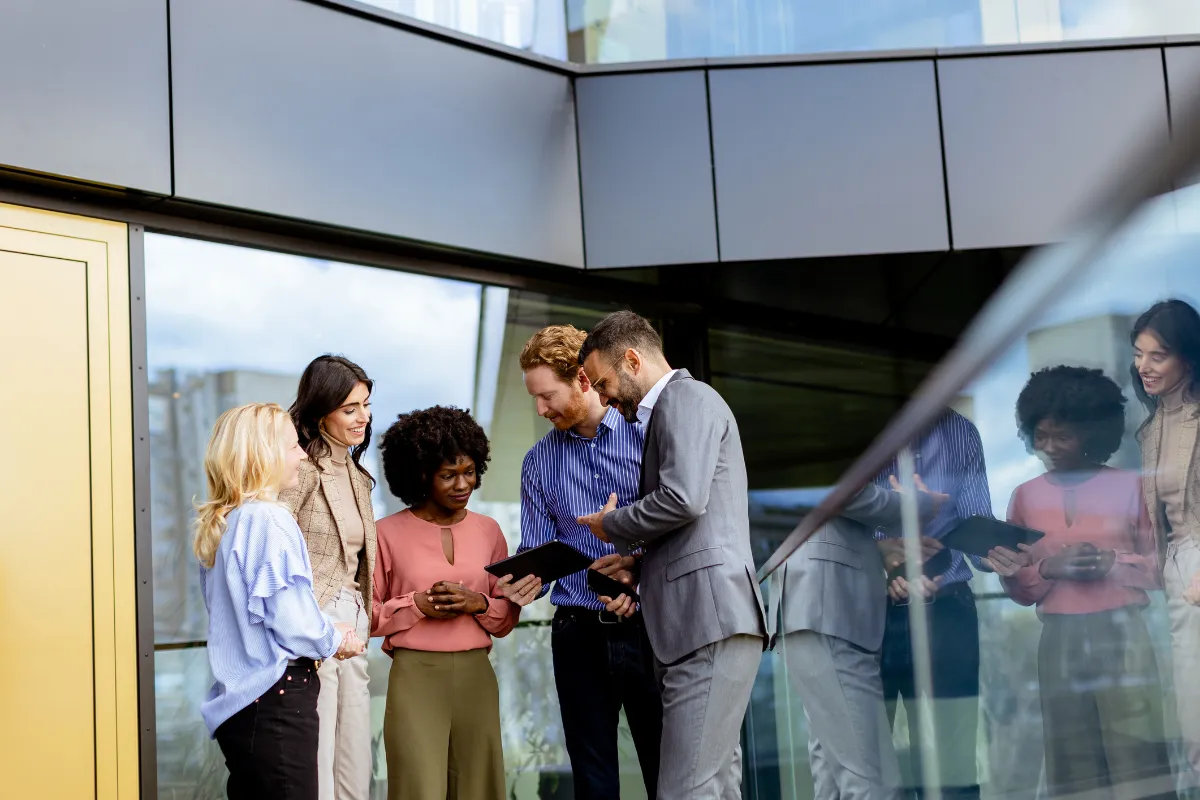 Grupo de profissionais reunidos conversando e analisando tablet em ambiente corporativo