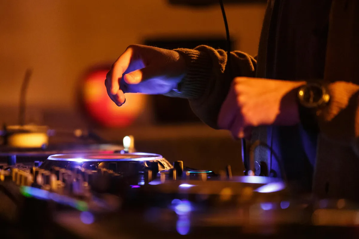DJ ajustando os controles de uma mesa de som iluminada durante evento noturno em ambiente fechado.